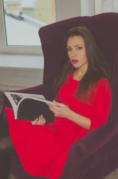Pencerenin önünde bir sandalyede çok güzel bir kız tarafından bir kitap okuma — Stok fotoğraf