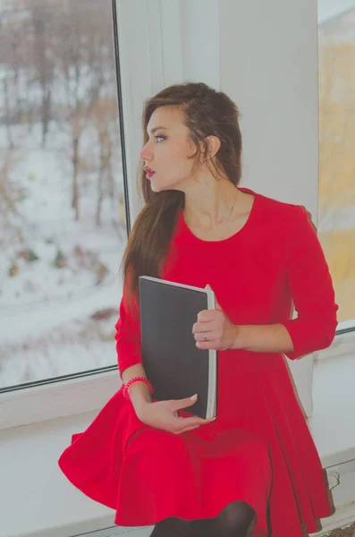 Bir kitapla pencereden güzel bir kız bir elbiseyle görünüyor — Stok fotoğraf