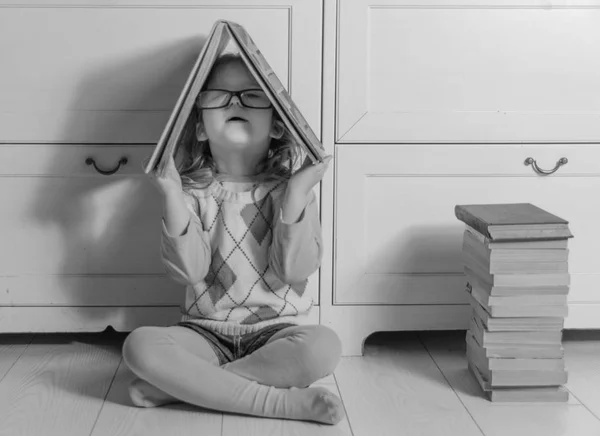 Uma casa de livro na cabeça da criança menina em óculos branco preto — Fotografia de Stock