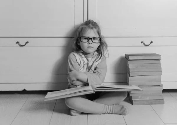 Black and white baby girl with a book in glasses upset — Stock Photo, Image