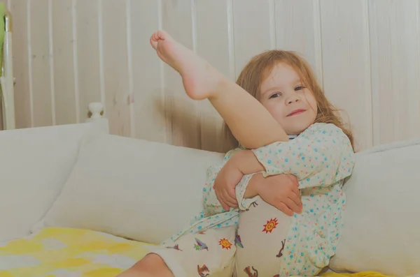 Yatağında bebek kız bacağını sarılmak oturur — Stok fotoğraf