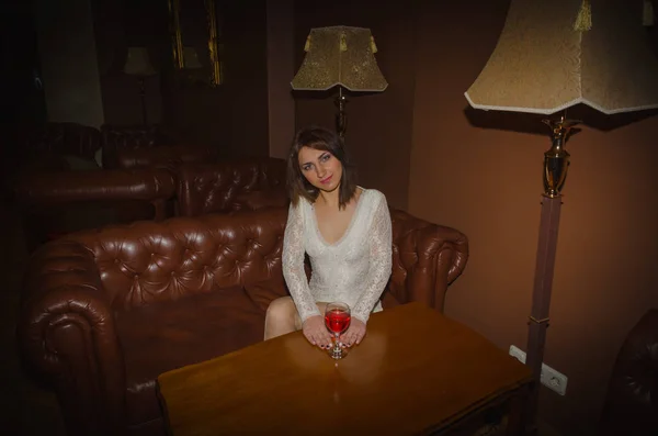 At a table in the lobby of the hotel sits a girl in a white dress with a glass of wine — Stock Photo, Image