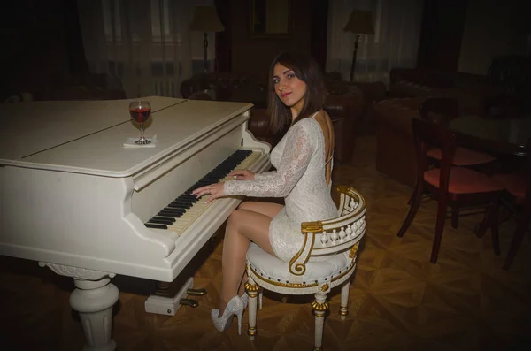 Κορίτσι με ένα λευκό φόρεμα με ένα ποτήρι κρασί στο πιάνο — Φωτογραφία Αρχείου
