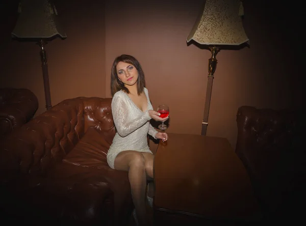 Chica en un vestido blanco con una copa de vino en el sofá —  Fotos de Stock