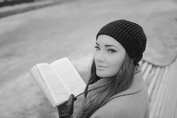 Preto e branco. menina interessante em um banco de parque com um livro — Fotografia de Stock