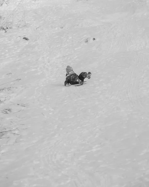 Schwarz-weiß, ein Kind, das im Winter auf dem Hügel reitet — Stockfoto