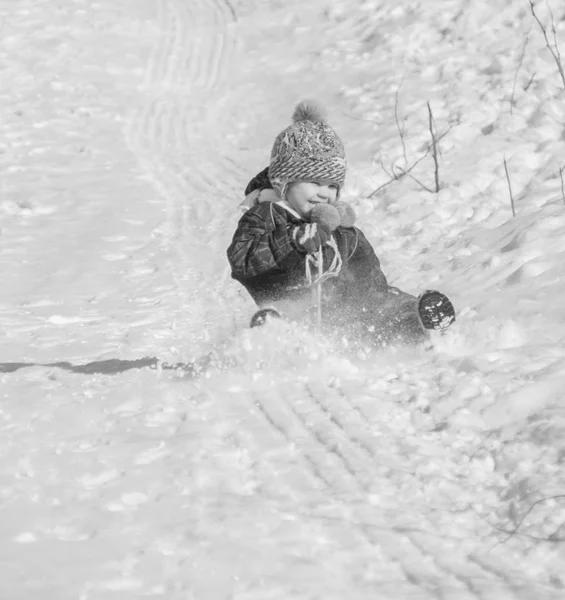 Schwarz-Weiß. ein Kind, das auf einem verschneiten Hügel aus nächster Nähe reitet — Stockfoto