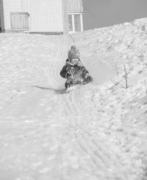 På vintern i närheten av huset av ett barn ridning kullarna på slädar, svart och vitt — Stockfoto