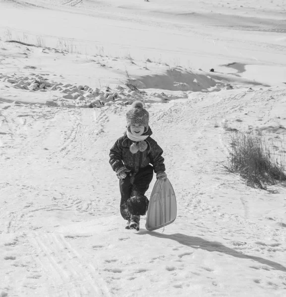 Glückliches Kind auf einem schneebedeckten Hügel auf einem Schlitten, schwarz-weiß — Stockfoto