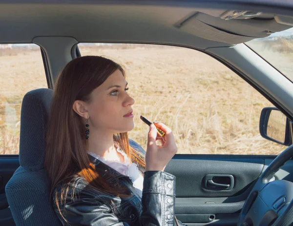 Hermosa chica en el coche poner en lápiz labial . — Foto de Stock