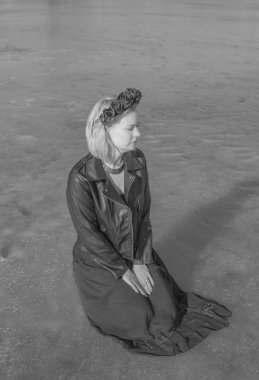 siyah-beyaz bir kız siyah çelenk içinde buz üstünde oturuyor.