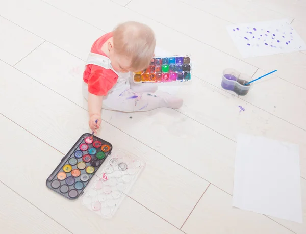 Dans une flaque d'eau se trouve un enfant avec des peintures et une brosse . — Photo