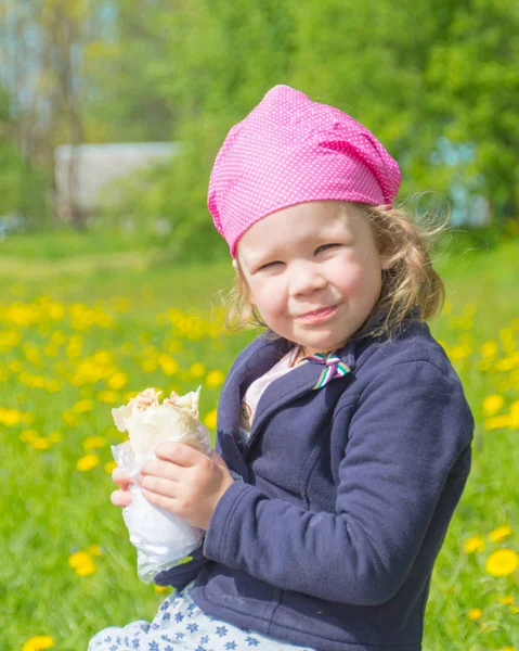 Fechar no parque um dia ensolarado uma criança come fast food . — Fotografia de Stock
