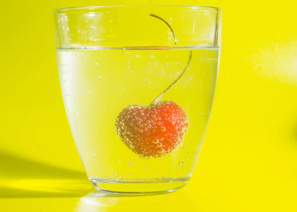 Close-up de cereja na água com bolhas em um fundo amarelo . — Fotografia de Stock