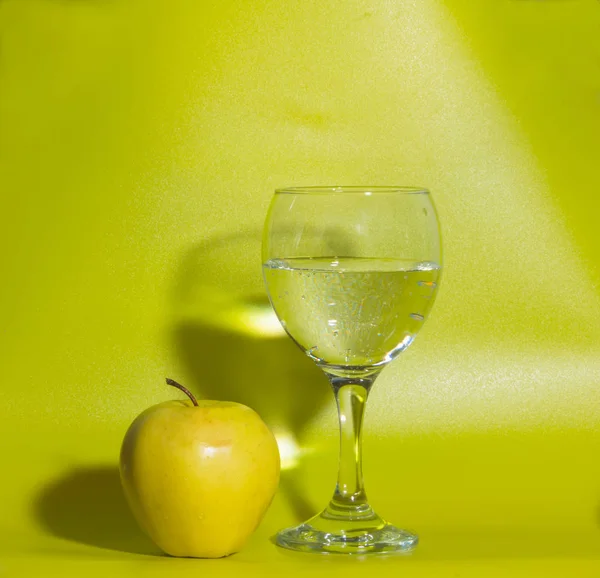 Un bicchiere d'acqua e una mela gialla su fondo verde . — Foto Stock