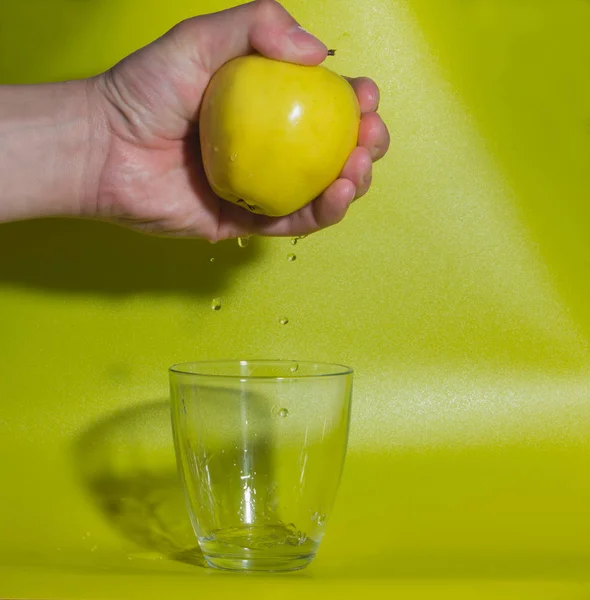 Mano con mela gialla, cadendo gocce in un bicchiere d'acqua . — Foto Stock