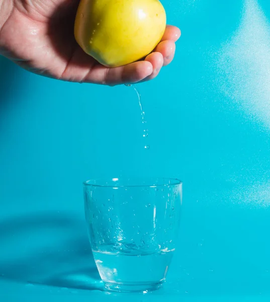 In a glass of water falling drops of water with Apple in hand. — Stock Photo, Image