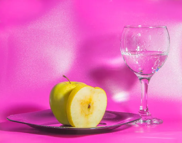 Sul piatto è giallo mela con un bicchiere d'acqua su un bac rosa — Foto Stock