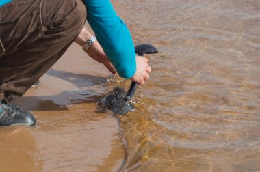 temiz su kumlu plajında bir adam kepçe yıkıyor.