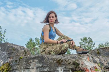 bir kız bir tabanca ile taş duvarda oturur.