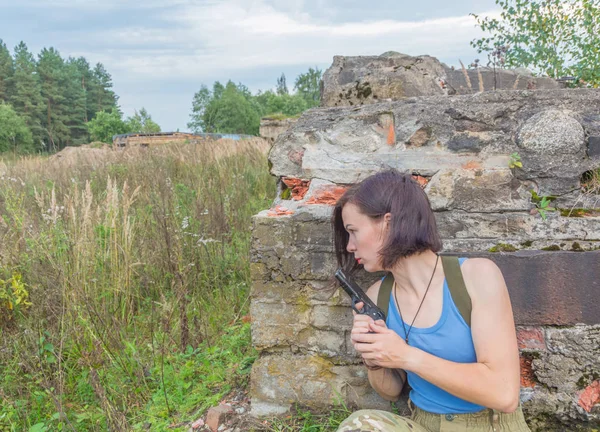Kız silahla beton bir duvarın arkasında saklanıyor.
