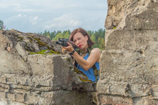 Дівчина з пістолетом прицілиться, стоїть за кам'яною стіною . — стокове фото