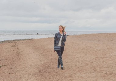 Bulutlu gün çekici bir kız sahilde yürüyor.