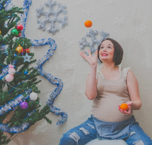 Bredvid trädet kastar gravid flicka apelsiner i det nya året — Stockfoto