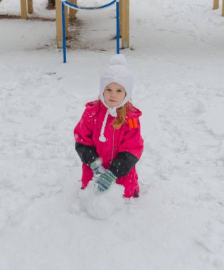 bir kız oyun alanında bir kardan adam kışın sculpts.