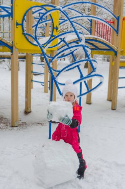 bir kız oyun alanında bir kardan adam kışın sculpts.