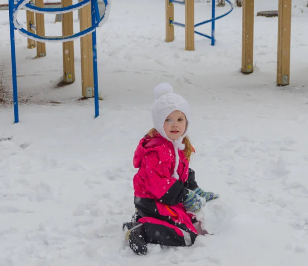 En flicka skulpterar en snögubbe på lekplatsen på vintern — Stockfoto