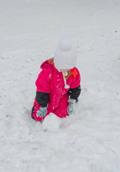 Uma menina esculpe um boneco de neve no parque infantil no inverno — Fotografia de Stock