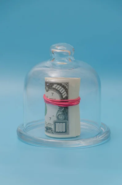 Ένα πακέτο δολάρια κάτω από ένα γυάλινο καπάκι, σε μπλε φόντο — Φωτογραφία Αρχείου