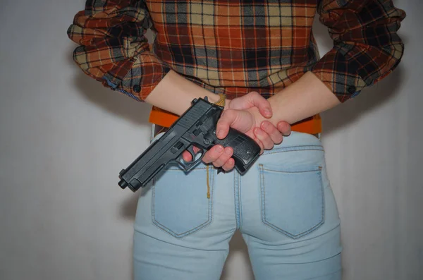 На сером фоне, девушка держит пистолет за своей бабой — стоковое фото