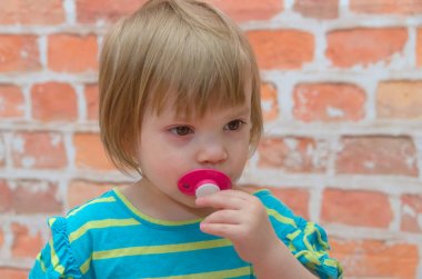 bir kız, bir çocuk bir emzik ile tuğla arka plan üzerinde eller.