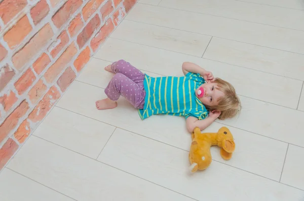 Een klein meisje, een kind met een fopspeen en speelgoed hert — Stockfoto