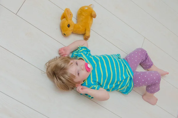 Een klein meisje, een kind met een fopspeen en speelgoed hert — Stockfoto
