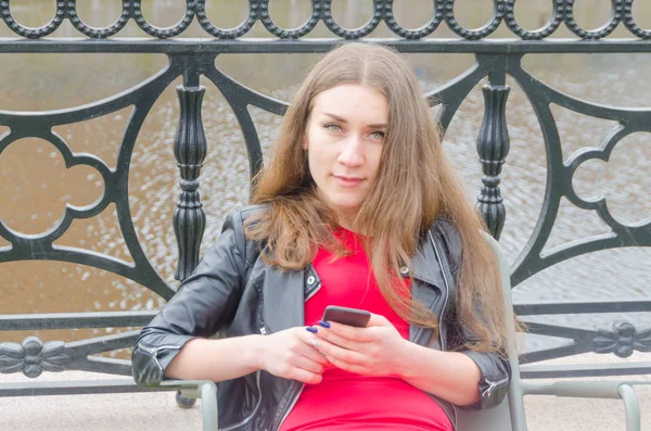 Niña en vestido y chaqueta de cuero con teléfono en la mano —  Fotos de Stock