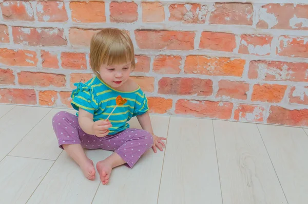 Przeciwko Cegły Ścienne Małą Dziewczynką Dziecko Zjada Cukierki Karmelowe Patyku — Zdjęcie stockowe
