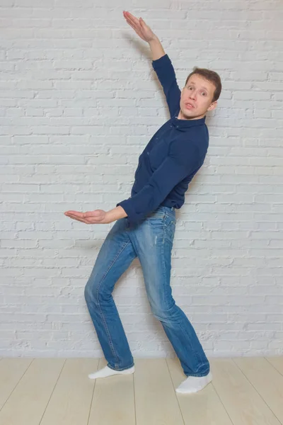 Man shows a gesture in front of a white brick wall — 图库照片