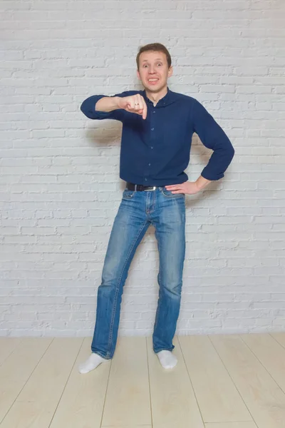 Man shows a gesture in front of a white brick wall — Stock Photo, Image