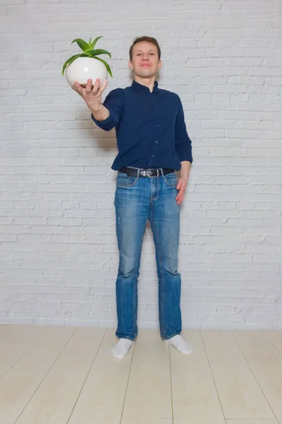 Man with a flower in a pot against a white brick wall expresses — 图库照片