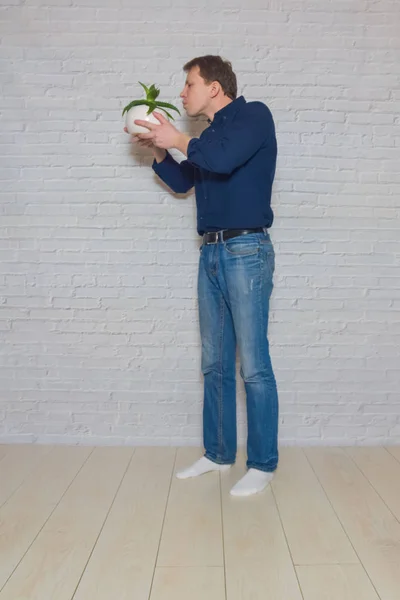 Mann mit einer Blume im Topf vor einer weißen Ziegelwand — Stockfoto