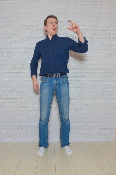 Man shows a gesture in front of a white brick wall — 图库照片