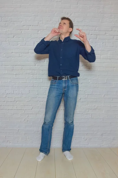 Uomo mostra un gesto davanti a un muro di mattoni bianchi — Foto Stock