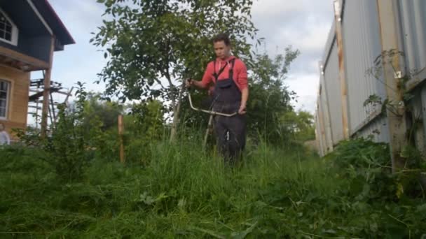 Een arbeider maait het gras met een trimmer in de tuin — Stockvideo