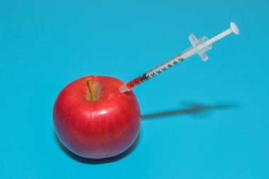 Mavi arka planda Apple 'da çekilen kimyasallarla dolu şırınga.