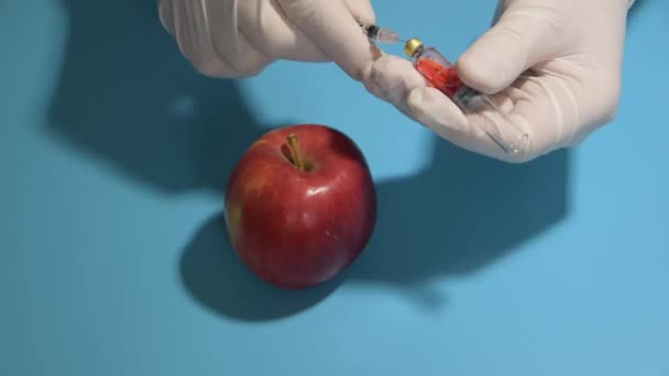 Σύριγγα με χημικά που έχουν πυροβοληθεί στο μήλο σε μπλε φόντο — Αρχείο Βίντεο
