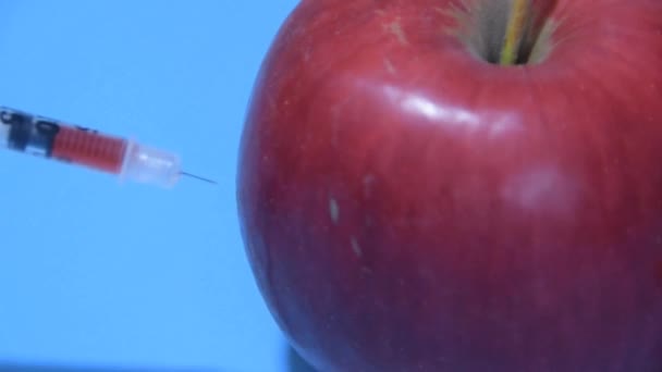 Jeringa con productos químicos inyectados en la manzana sobre un fondo azul — Vídeos de Stock