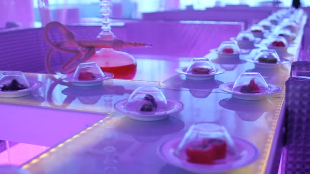 Plates with different sushi go around the conveyor belt in neon light. — Stock Video
